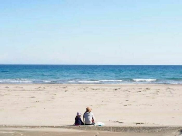 青い海と空の下白い砂浜に座る親子2人