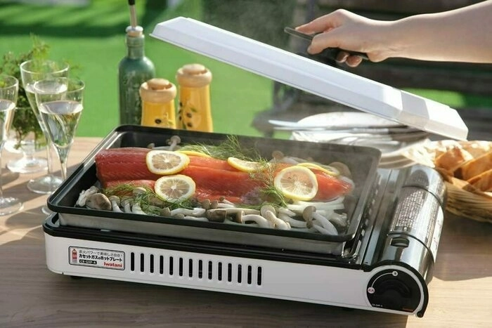 カセットコンロに鮭やキノコの具材を並べ屋外で焼いている